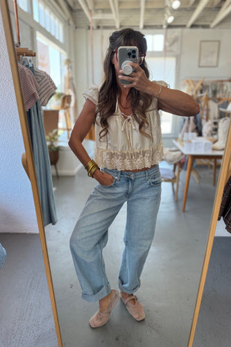 Person taking a mirror selfie wearing a beige top and light blue jeans in a clothing store.