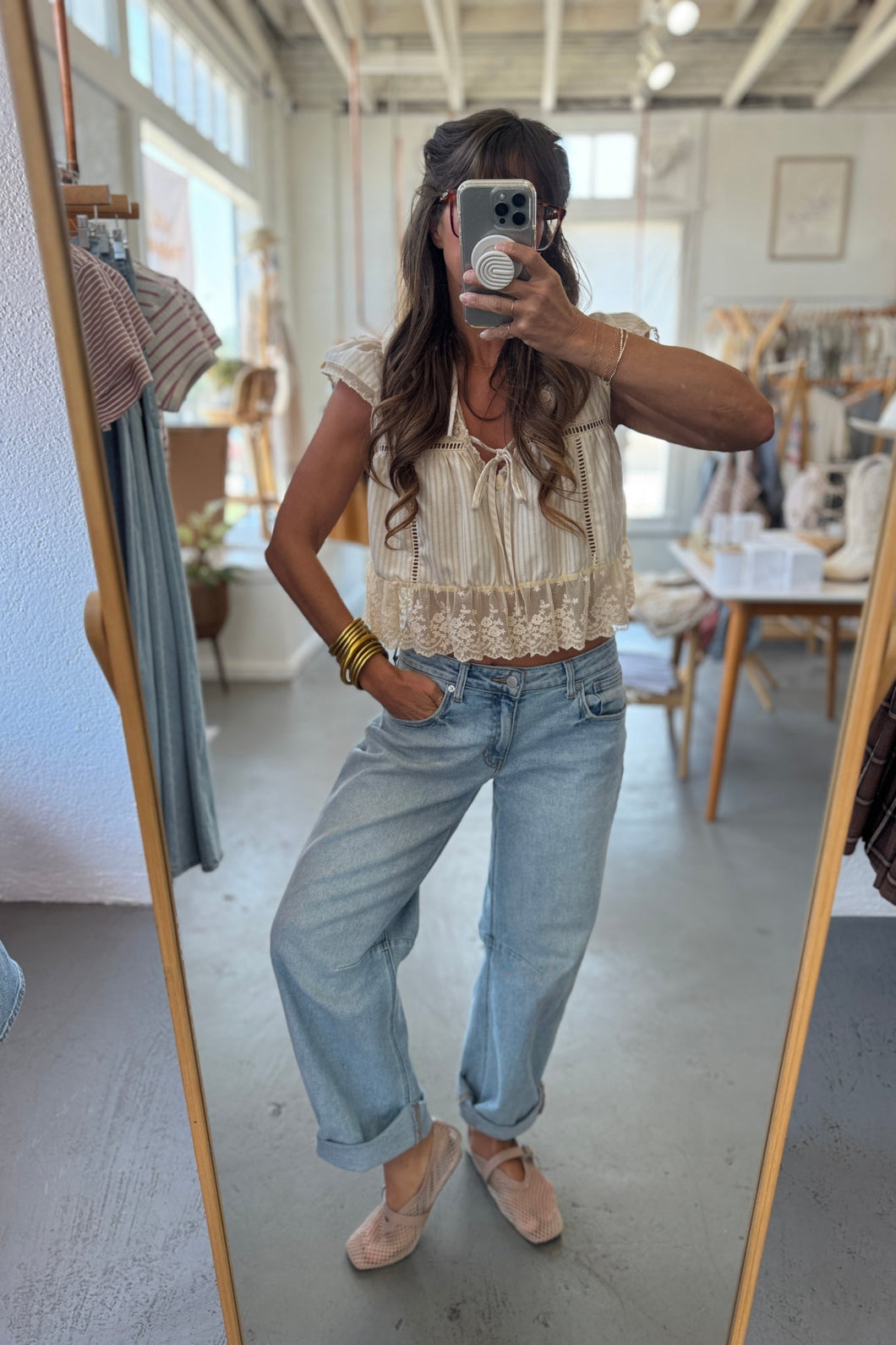 Person taking a mirror selfie wearing a beige top and light blue jeans in a clothing store.