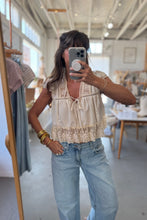 Load image into Gallery viewer, Woman taking a mirror selfie wearing a beige top and light blue jeans in a store.