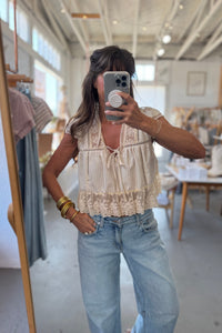 Woman taking a mirror selfie wearing a beige top and light blue jeans in a store.