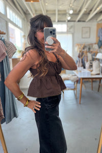 Woman taking a mirror selfie wearing a brown top and black pants in a store.