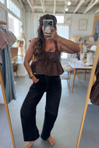 Person taking a mirror selfie wearing a brown top and black pants in a clothing store.