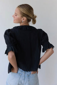 Woman wearing a black blouse with ruffled sleeves against a plain background