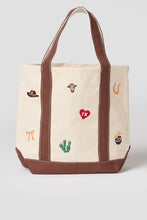 Load image into Gallery viewer, A cream canvas tote bag with brown leather-look trim and handles, decorated with small embroidered western-themed motifs including a cowboy hat, longhorn, horseshoe, cactus, and heart.