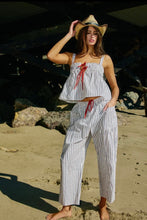 Load image into Gallery viewer, Woman in a striped outfit and straw hat standing on a beach.