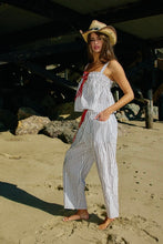 Load image into Gallery viewer, Woman in a striped outfit and cowboy hat standing on a sandy beach.