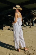Load image into Gallery viewer, Woman in a striped jumpsuit and straw hat standing on a sandy beach.