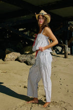 Load image into Gallery viewer, Woman in a striped outfit and cowboy hat standing on a sandy beach.