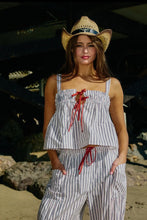 Load image into Gallery viewer, Woman wearing a striped outfit and cowboy hat on a beach.