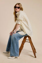 Load image into Gallery viewer, Woman sitting on a wooden stool wearing a polka dot blouse and jeans against a beige background