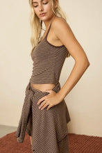 Load image into Gallery viewer, A woman modeling a brown and beige striped two-piece set consisting of a halter crop top and a matching wrap-style skirt, set against a plain beige wall.