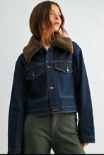 Load image into Gallery viewer, A woman wearing a cropped dark blue denim jacket with a brown shearling-style collar, paired with olive green pants, photographed against a plain light gray studio background.