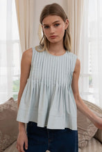 Load image into Gallery viewer, Woman wearing a light blue sleeveless top in a room with curtains and a couch.