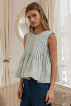 Load image into Gallery viewer, Woman wearing a light green pleated top and blue jeans in an elegant interior setting.
