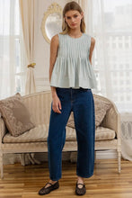Load image into Gallery viewer, Woman wearing a light blue sleeveless top and blue jeans standing in a room with a beige sofa and decorative mirror.