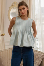 Load image into Gallery viewer, Woman wearing a light green pleated top and blue jeans in a room with a mirror and window.