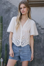 Load image into Gallery viewer, Woman wearing a white blouse with lace details and denim shorts standing against a textured wall.