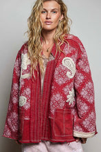 Load image into Gallery viewer, A woman wearing a red and white paisley patterned jacket with lace appliques, photographed against a plain light gray studio background.
