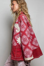 Load image into Gallery viewer, A woman shown in side profile wearing a red patchwork jacket with white paisley and floral prints, cream contrast stitching, and frayed cuffs, paired with distressed gray pants against a plain gray studio background.
