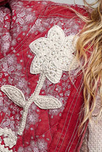 Load image into Gallery viewer, A close-up of a red quilted fabric with a white paisley pattern and a large white crocheted flower applique, with blonde hair visible on the right side.