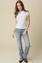 Load image into Gallery viewer, Woman wearing a white blouse with black polka dots and blue jeans on a beige background