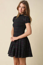 Load image into Gallery viewer, A woman modeling a short puff-sleeve dress with a dark green and black plaid pattern and thin red stripes, set against a plain beige background.
