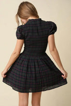 Load image into Gallery viewer, A woman shown from the back wearing a short puff-sleeve plaid dress in a dark green and black tartan pattern with thin red lines, set against a plain beige background.