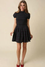 Load image into Gallery viewer, A woman modeling a short puff-sleeve plaid dress with a gathered waist and flared skirt, paired with red pointed-toe heels, against a plain beige studio background.