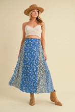 Load image into Gallery viewer, Woman wearing a blue floral skirt with a beige top and hat on a beige background