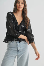 Load image into Gallery viewer, Woman wearing a black floral blouse and light blue jeans on a white background
