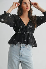Load image into Gallery viewer, Woman wearing a black floral blouse and light blue jeans on a plain background