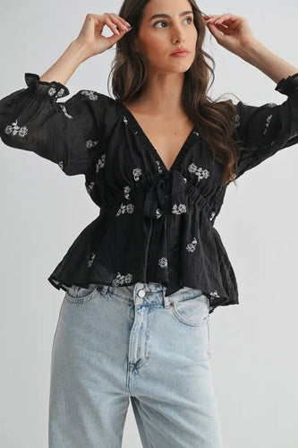 Woman wearing a black floral blouse and light blue jeans on a plain background