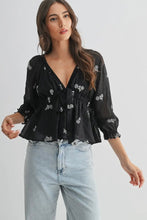 Load image into Gallery viewer, Woman wearing a black floral blouse and light blue jeans on a white background
