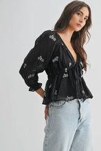 Load image into Gallery viewer, Woman wearing a black embroidered blouse and light blue jeans on a white background