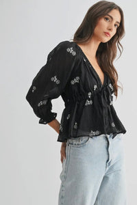 Woman wearing a black embroidered blouse and light blue jeans on a white background