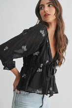 Load image into Gallery viewer, Woman wearing a black embroidered blouse with light blue jeans on a white background