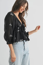 Load image into Gallery viewer, Woman wearing a black embroidered blouse and light blue jeans on a white background