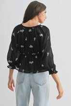 Load image into Gallery viewer, Woman wearing a black floral blouse and light blue jeans on a white background