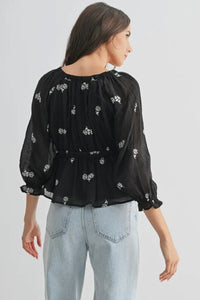 Woman wearing a black floral blouse and light blue jeans on a white background