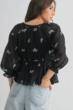 Load image into Gallery viewer, Woman wearing a black floral blouse and light blue jeans against a white background