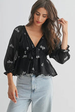 Load image into Gallery viewer, Woman wearing a black floral blouse and light blue jeans on a plain background