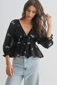 Woman wearing a black floral blouse and light blue jeans on a plain background