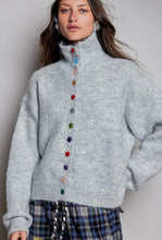 Load image into Gallery viewer, A woman wearing a light gray fuzzy turtleneck sweater with a vertical row of colorful decorative buttons down the front, paired with blue plaid pants, against a plain light gray background.
