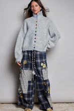 Load image into Gallery viewer, A model wearing a light gray mock-neck knit sweater with colorful buttons and a blue plaid patchwork wide-leg pant with floral details, standing against a neutral gray wall.