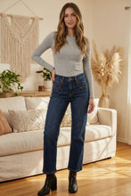 Load image into Gallery viewer, Woman standing in a living room wearing a gray long-sleeve top and blue jeans.