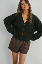 Load image into Gallery viewer, Woman wearing a dark green cardigan with brown buttons and plaid shorts on a plain background