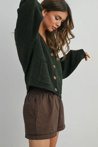 Woman wearing a green cardigan and plaid skirt on a plain background