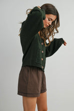 Load image into Gallery viewer, Woman wearing a green cardigan and brown checkered shorts on a plain background