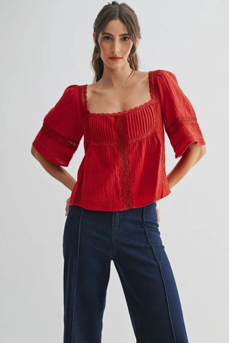Woman wearing a red blouse with puffed sleeves and blue pants on a white background