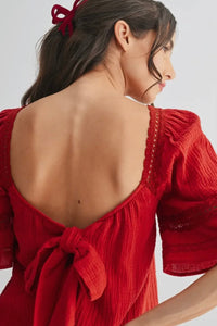 Woman wearing a red dress with an open back and puffed sleeves on a white background
